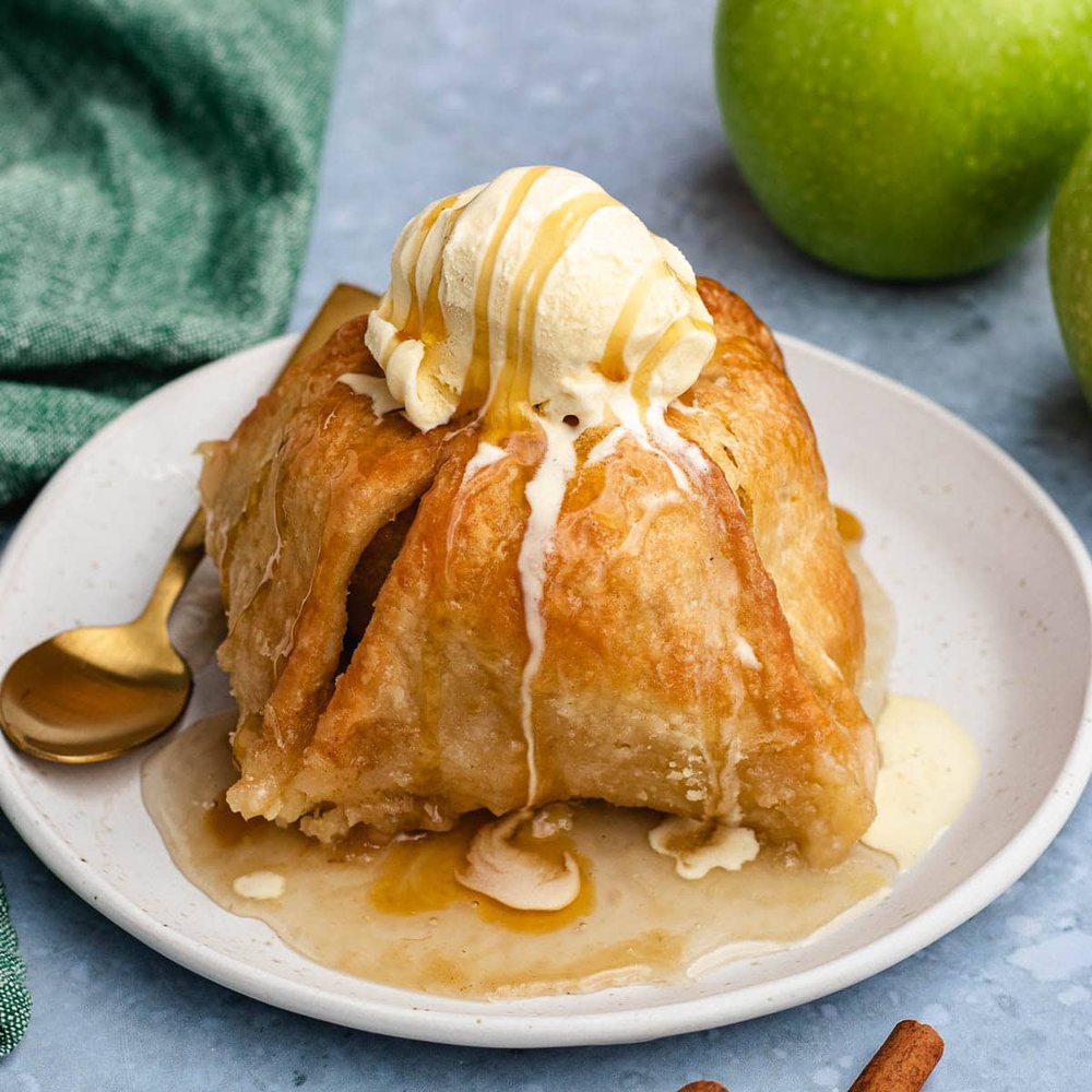 A baked apple dumpling topped with a scoop of vanilla ice cream and caramel